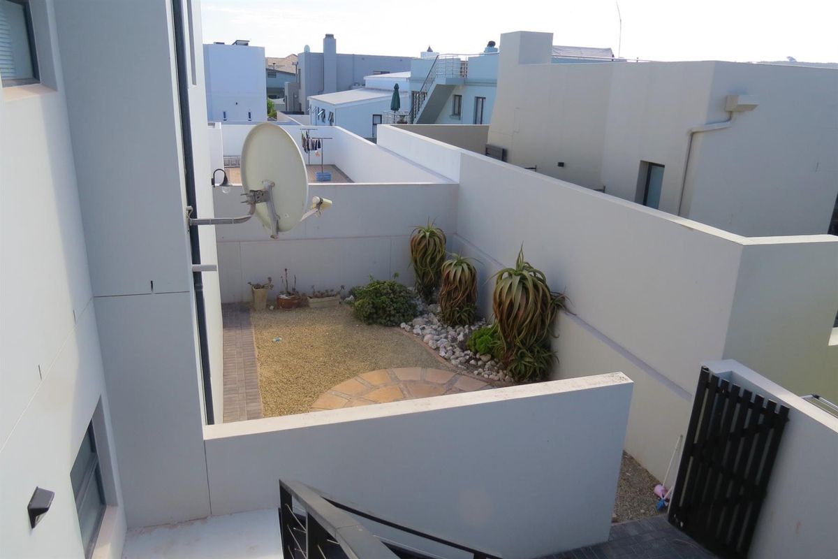 An elevated view of a private courtyard garden featuring paved sections, gravel landscaping, and established succulent plants, enclosed by high boundary walls.