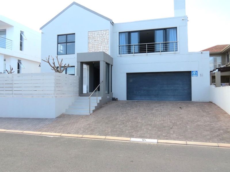 Modern double-story residential facade featuring a paved driveway, integrated double garage, stone cladding detail, and an elevated balcony with stainless steel railings.