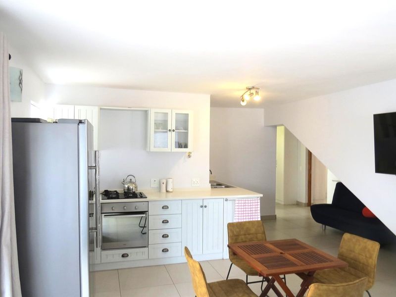 Open plan kitchen featuring white cabinetry, built-in oven, gas hob, and tiled flooring, seamlessly flowing into the adjacent living area.
