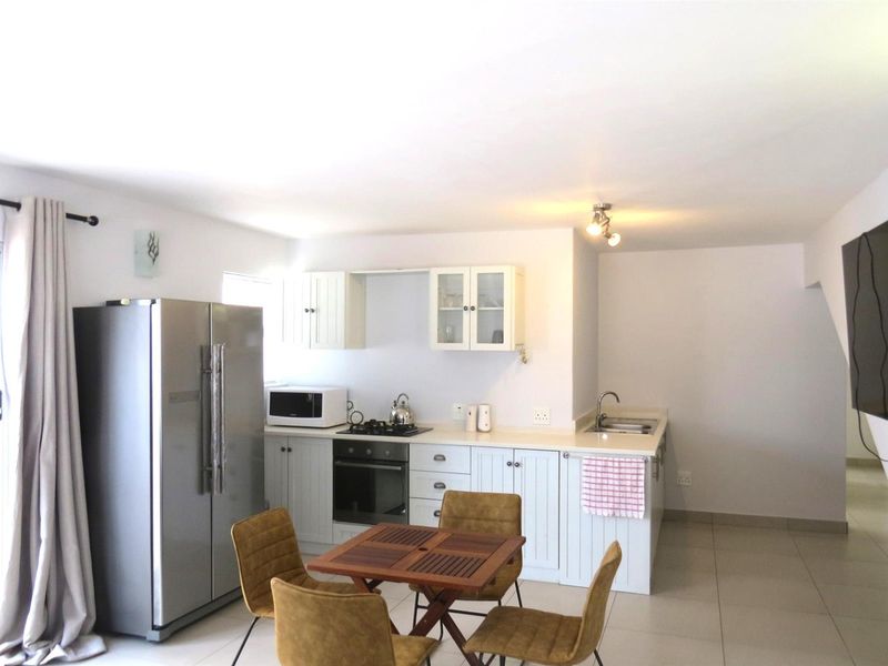 Open-plan kitchen featuring light-toned cabinetry, built-in oven, gas hob, and a stainless steel sink, seamlessly integrated with the dining area.