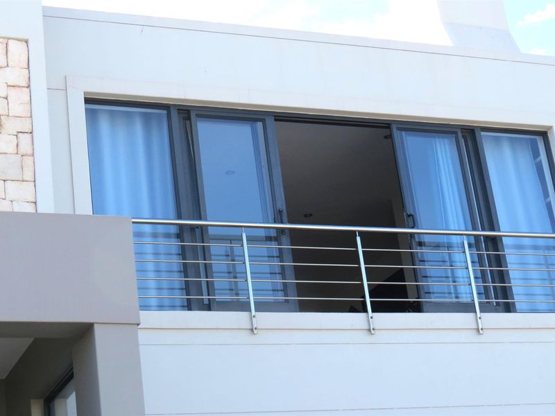 A modern upper-level balcony featuring a stainless steel railing and large sliding glass doors providing access to the interior.