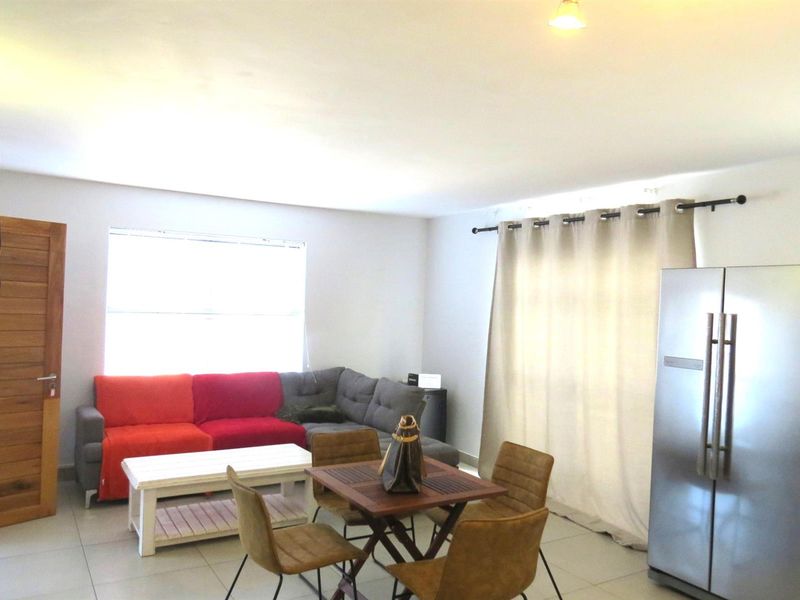An open-plan living and dining area featuring tiled flooring, a wooden door, and large windows with curtain rods.
