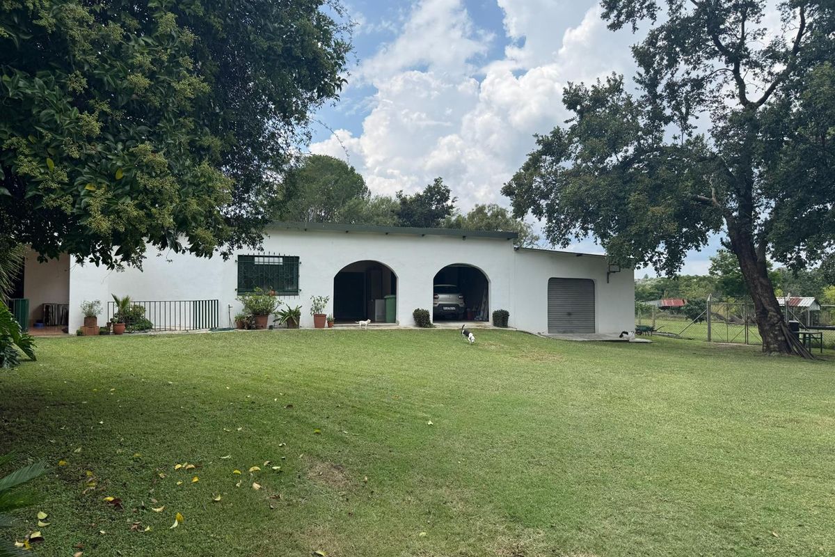 A view of the rear exterior of the small holding, featuring arched openings, a garage door, and a spacious lawn area.