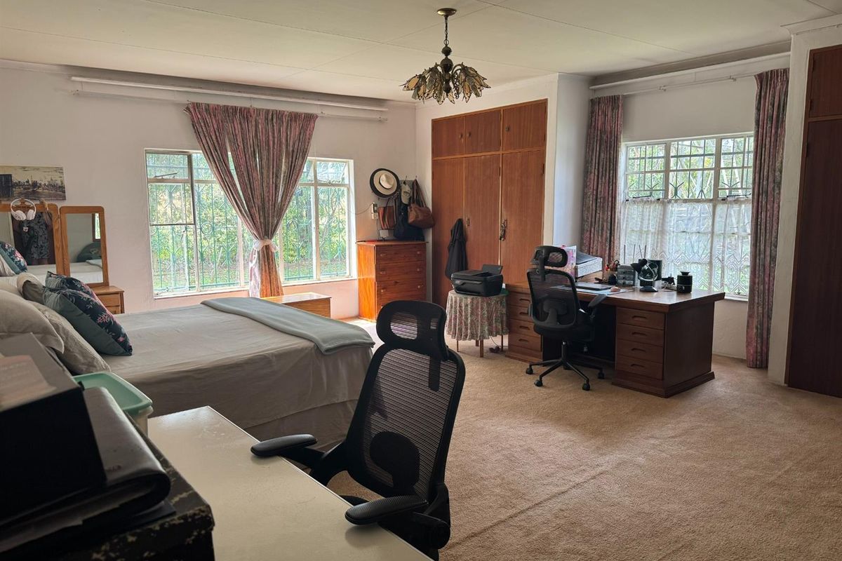 Spacious bedroom featuring built-in wooden cupboards, large windows with security bars, and neutral carpeting.
