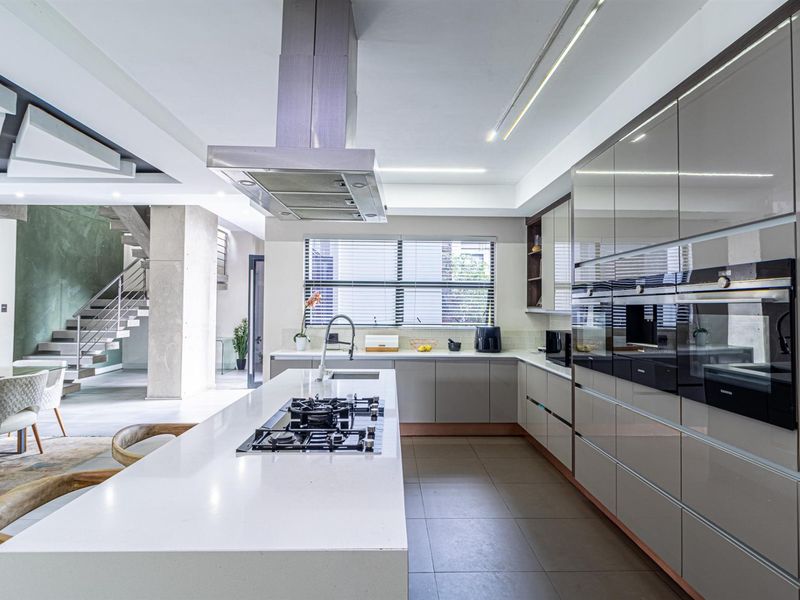 Modern open-plan kitchen featuring high-gloss cabinetry, stone countertops, a central island with gas cooktop, and integrated appliances, seamlessly connecting to the living area.