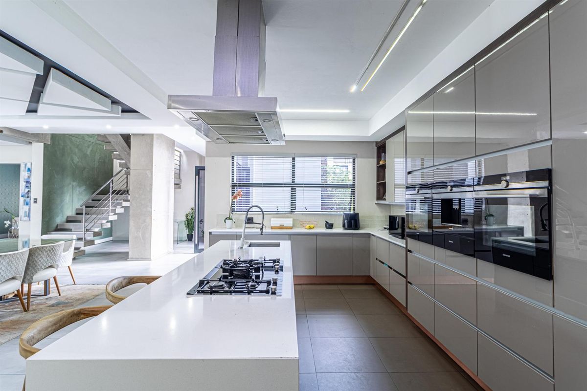 Modern open-plan kitchen featuring high-gloss cabinetry, stone countertops, a central island with gas cooktop, and integrated appliances, seamlessly connecting to the living area.