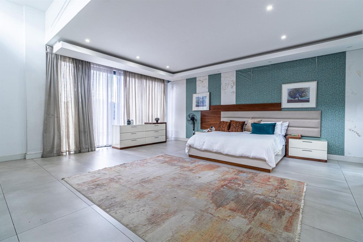 Spacious bedroom featuring large-format floor tiles, recessed ceiling lighting, and a custom built-in headboard with decorative wallpaper accents.