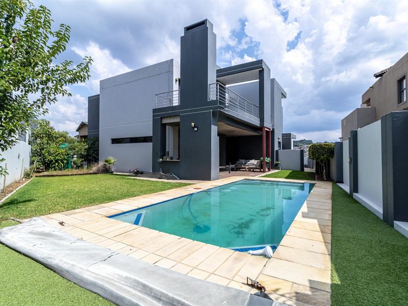 Rear exterior view featuring a swimming pool, covered patio, balcony, and outdoor fireplace set within a private garden with boundary walls.