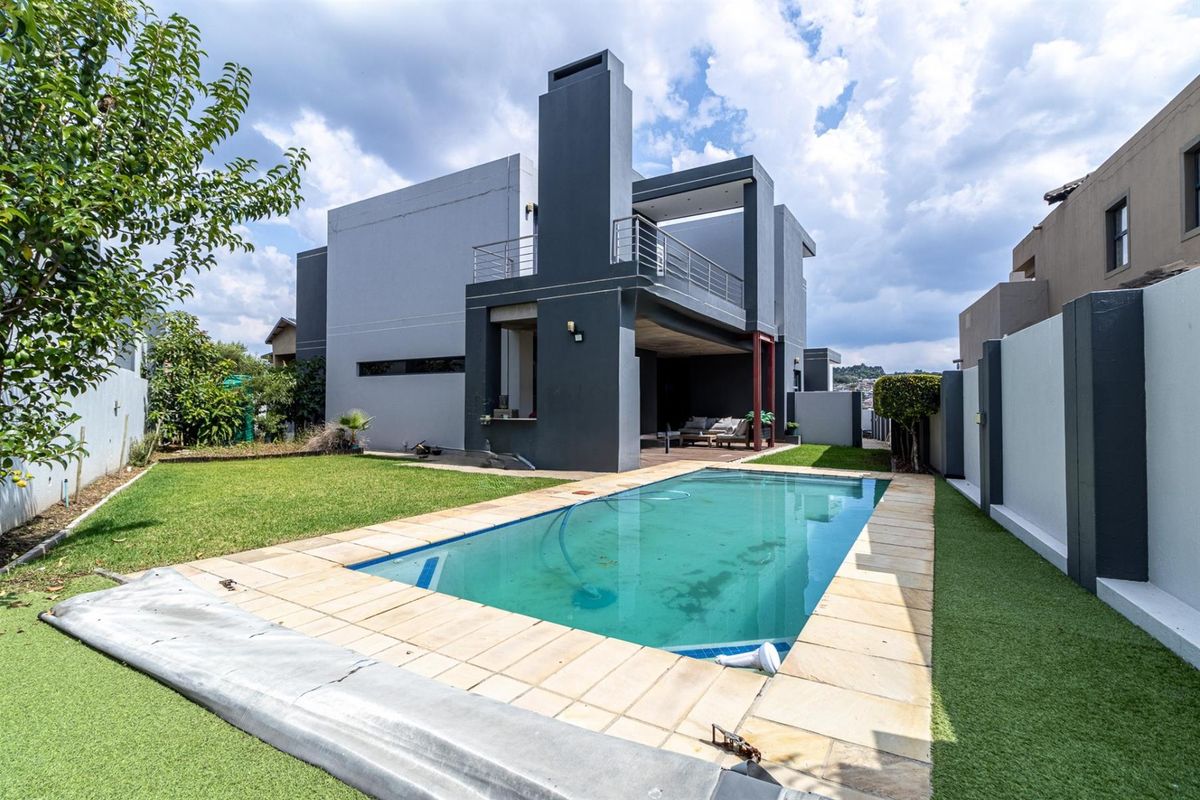 Rear exterior view featuring a swimming pool, covered patio, balcony, and outdoor fireplace set within a private garden with boundary walls.