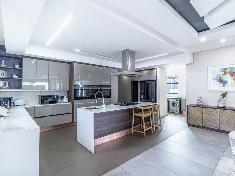 Modern open-plan kitchen featuring a central island with gas cooktop, high-gloss cabinetry, integrated appliances, and sleek tiled flooring with recessed ceiling lighting.