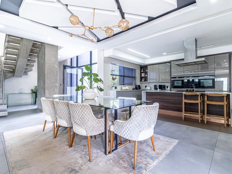 Modern open-plan living area featuring a sleek kitchen with built-in appliances, a dining space, and a striking architectural concrete staircase.