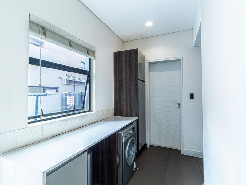 A functional laundry room featuring built-in cabinetry, stone countertops, tiled flooring, and a window providing natural light.