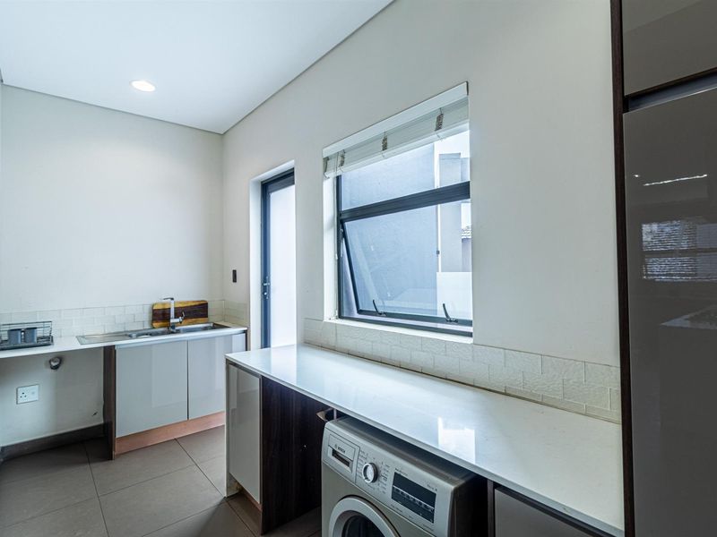 A clean and functional laundry room featuring built-in cabinetry, stone countertops, a stainless steel sink, and tiled flooring with direct outdoor access.