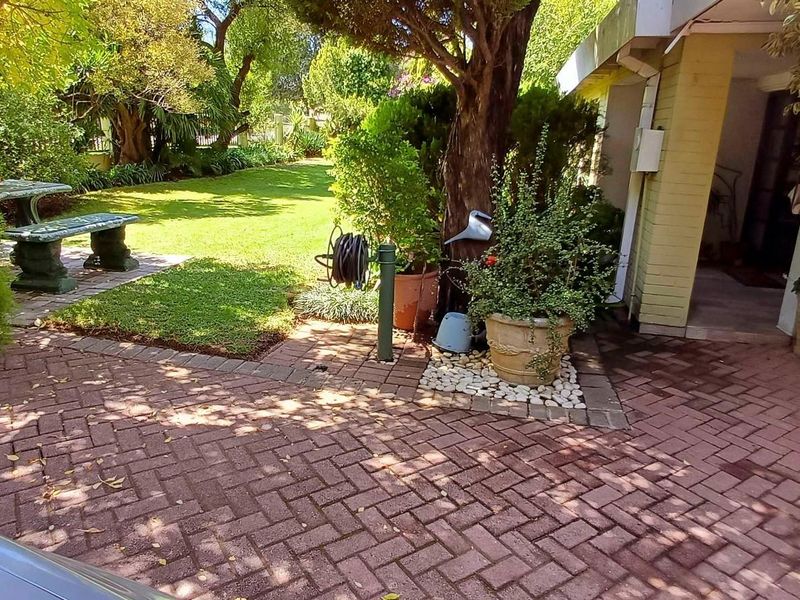 A well-maintained garden area featuring brick paving, established trees, and a lush lawn leading to the home's entrance.