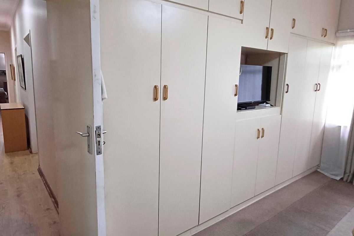 A bedroom featuring extensive built-in cupboards with integrated shelving and laminate flooring, leading into a hallway.