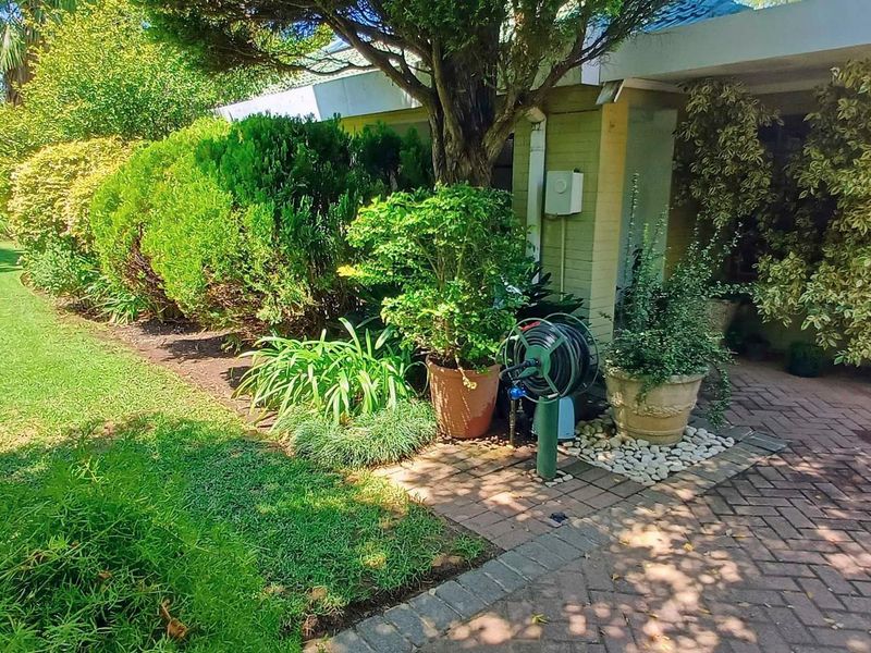A well-maintained front entrance featuring a brick paved walkway, established garden beds, and a classic timber front door.