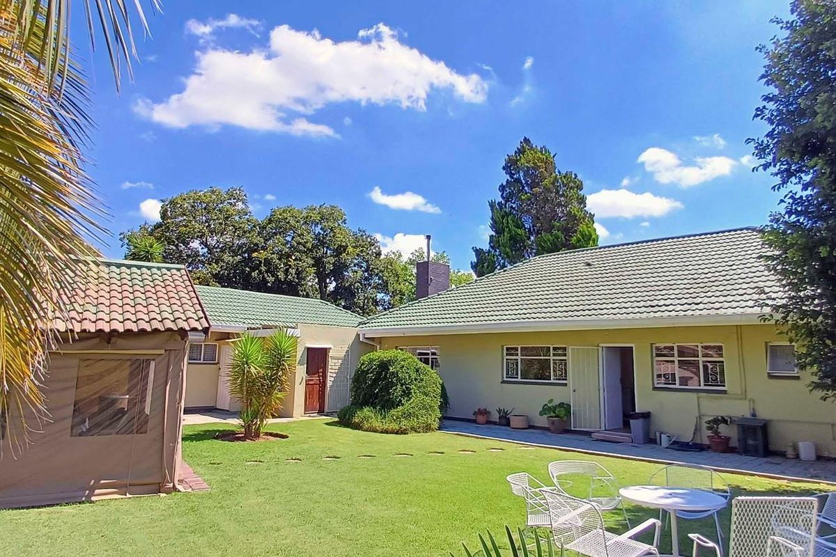 A view of the rear garden featuring a well-maintained lawn, paved patio area, and the rear elevation of the house with a tiled roof.