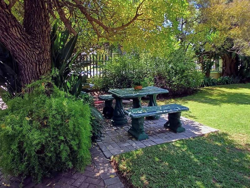 A well-maintained garden area featuring mature trees, a paved section, and a metal perimeter fence, providing a pleasant outdoor space.