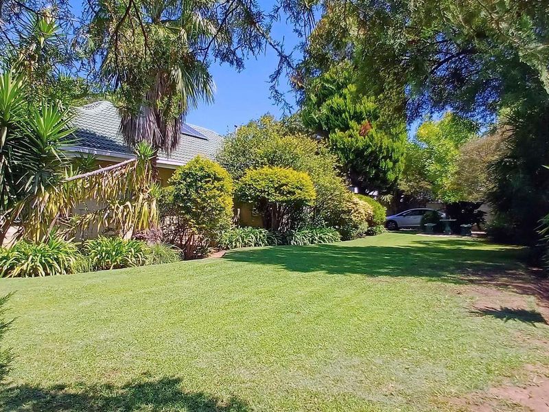 A well-maintained residential garden featuring a lush lawn, mature trees, and established shrubbery alongside the side elevation of the house.