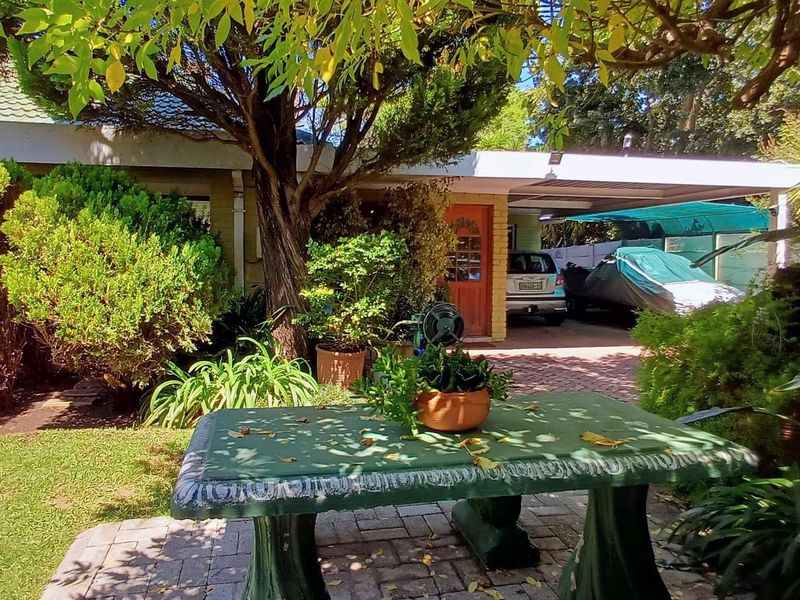 Front exterior view of the house featuring a paved driveway, carport, and established garden with mature trees.