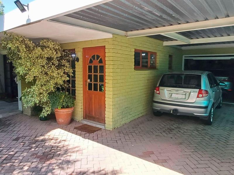 Front exterior view featuring a paved driveway, covered carport, and garage access with a painted brick facade.