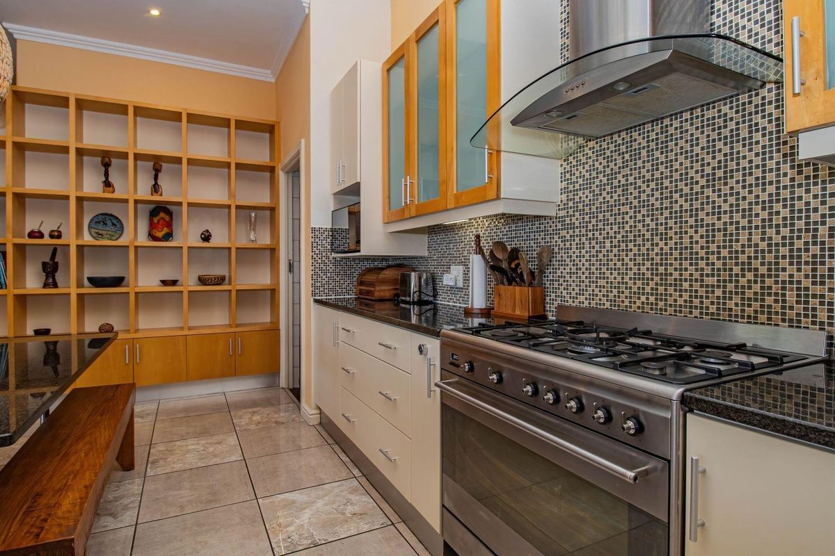 A well-appointed kitchen featuring granite countertops, a gas stove with extractor fan, mosaic tile backsplash, and extensive built-in wooden shelving.