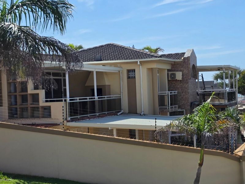 A view of the rear exterior of the house, featuring multi-level covered patios, stone cladding accents, and a perimeter wall with electric fencing.
