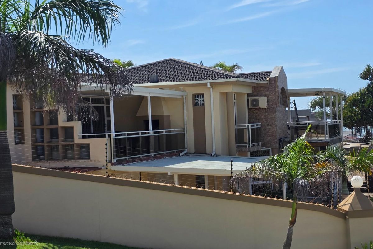 A view of the rear exterior of the house, featuring multi-level covered patios, stone cladding accents, and a perimeter wall with electric fencing.