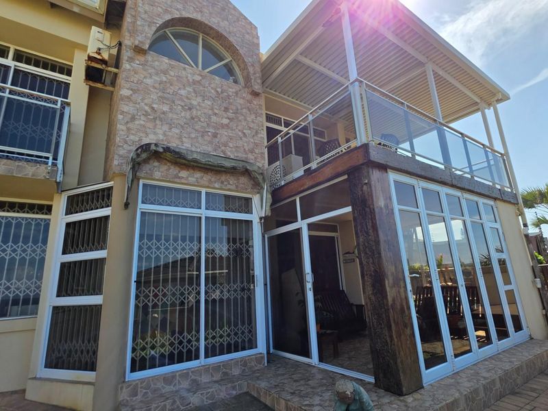 Rear exterior view featuring a covered patio with glass balustrades, stone-clad architectural detailing, and extensive sliding door access to the main dwelling.