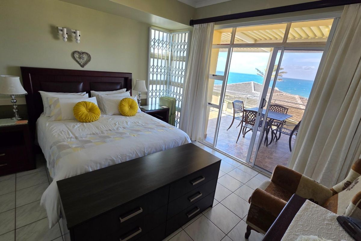 Spacious bedroom featuring tiled flooring, built-in wall lighting, and large sliding glass doors opening onto a private balcony with ocean views.