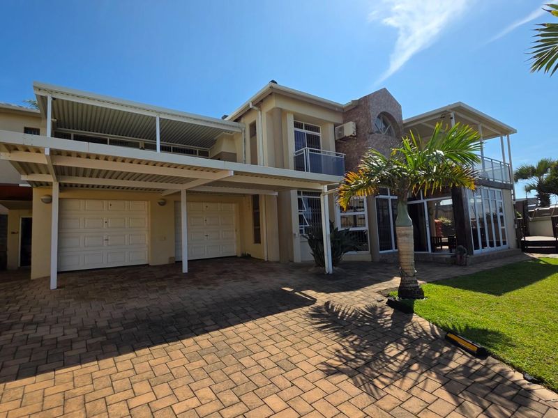 A spacious double-story residential property featuring a paved driveway, double garage, covered patio areas, and a well-maintained front garden.