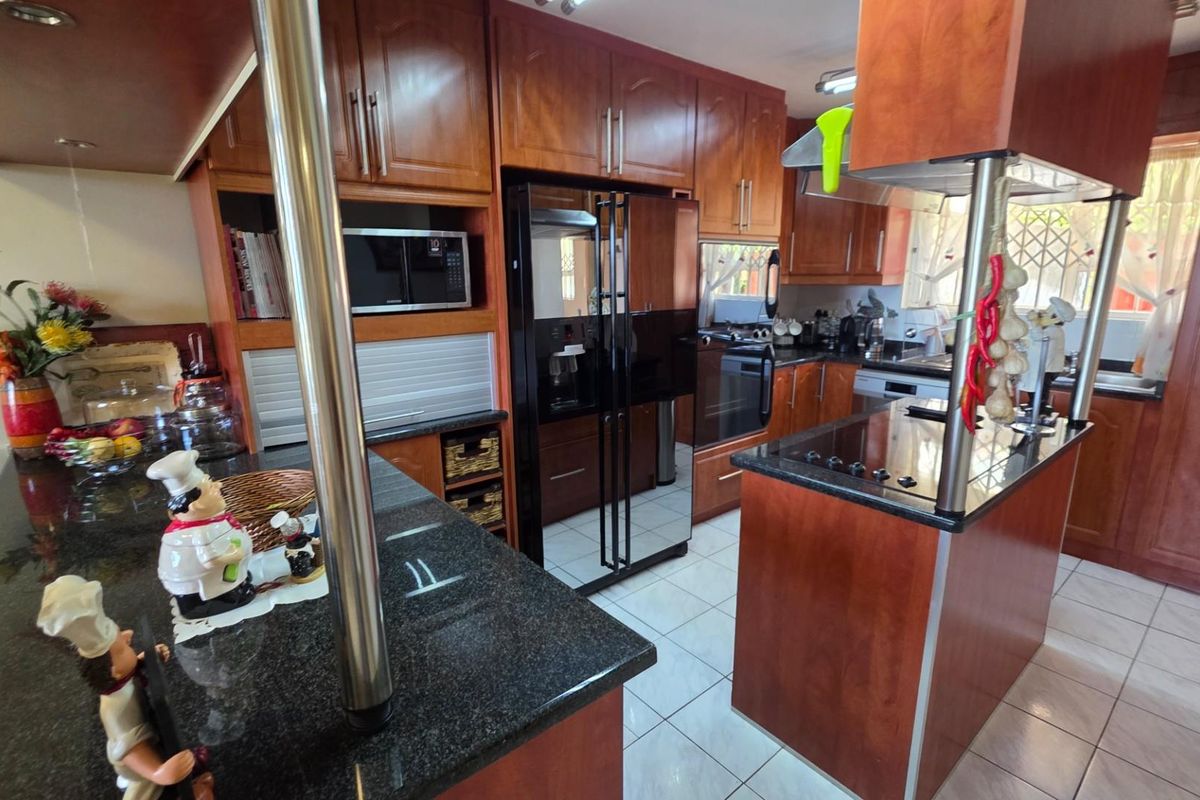 A functional kitchen featuring dark wood cabinetry, granite countertops, a central island with a built-in cooktop, and tiled flooring.