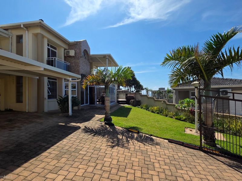 A well-maintained front exterior view featuring a paved driveway, covered carport, landscaped lawn, and a secure gated entrance.