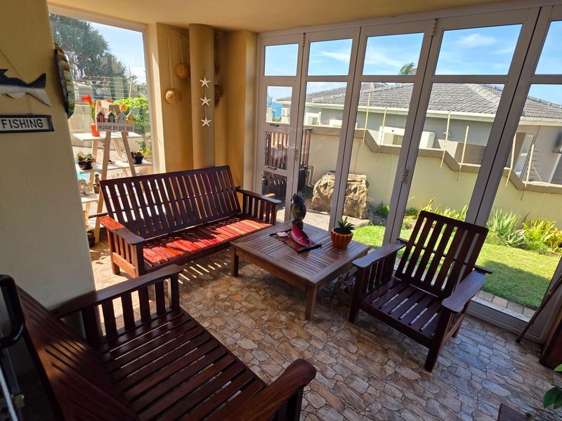 A bright, enclosed patio featuring stone-tiled flooring and large glass folding doors that provide seamless access to the garden and ocean views.
