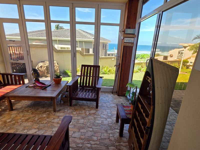 A sunroom featuring large glass folding doors, stone-tiled flooring, and expansive views of the surrounding coastal landscape.
