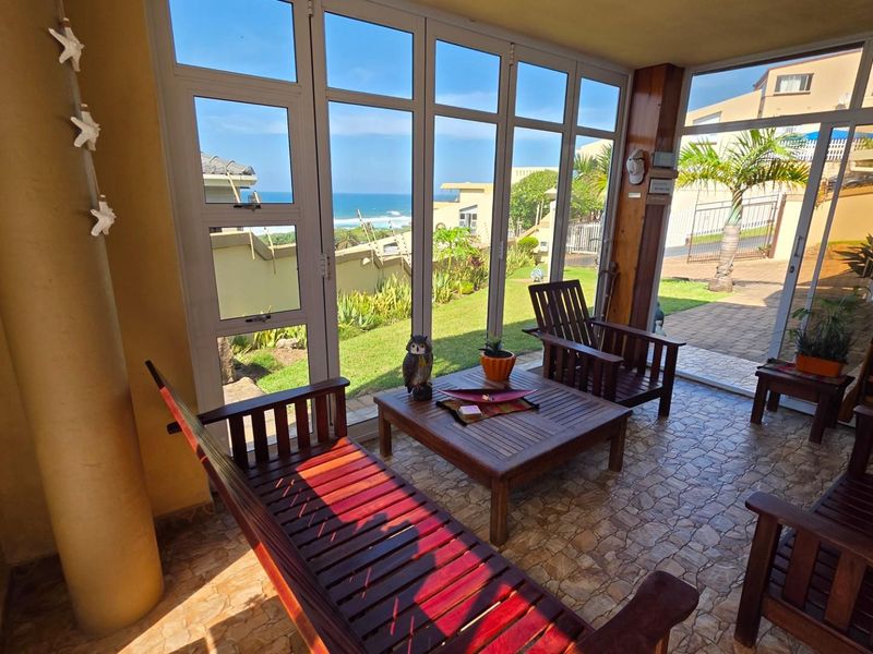 A sun-drenched enclosed patio featuring tiled flooring and expansive glass doors that provide seamless access to the garden and ocean views.