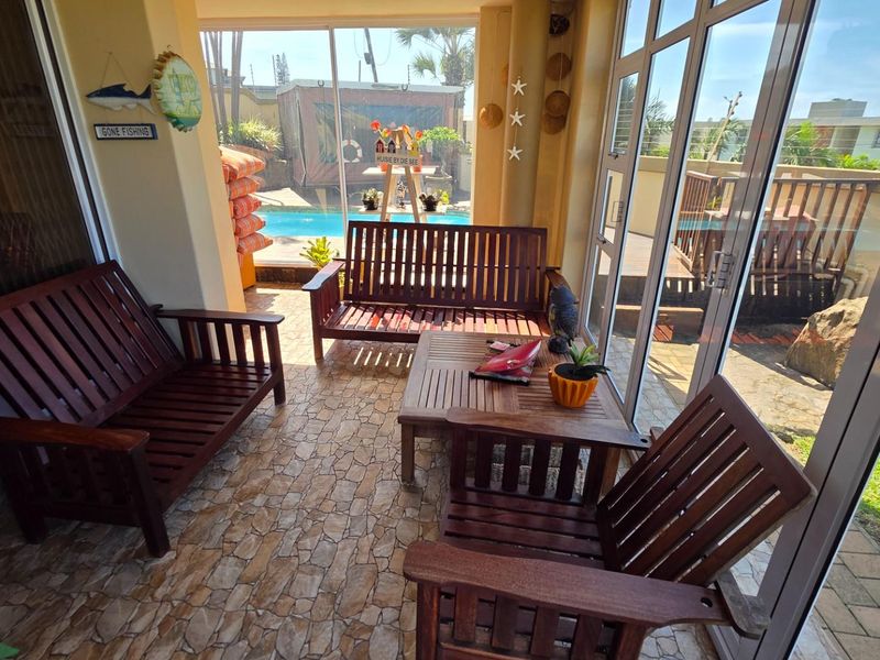 A covered patio area featuring stone-tiled flooring and large glass sliding doors, providing direct access and views to the outdoor swimming pool area.