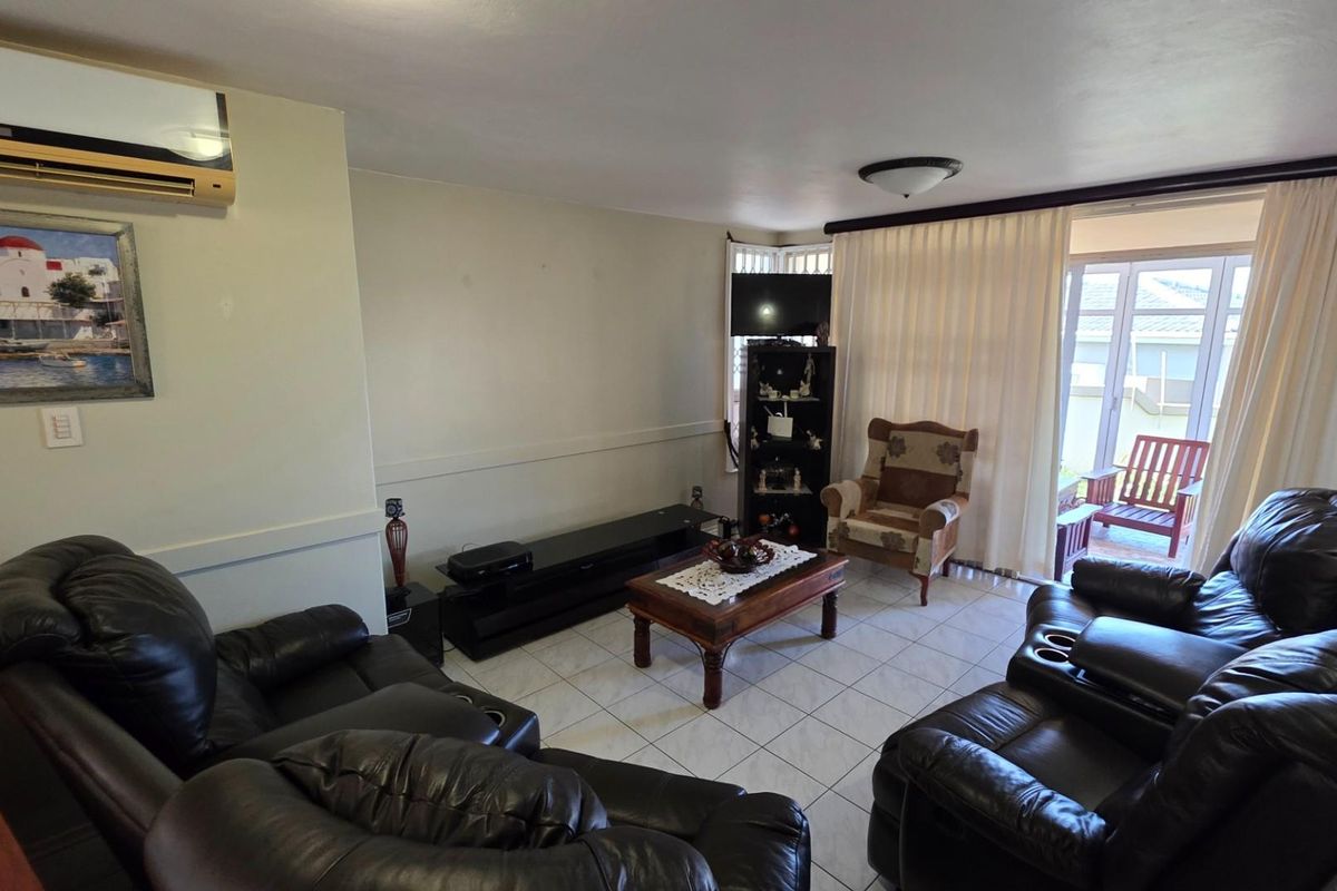 A comfortable living room featuring tiled flooring, a wall-mounted air conditioning unit, and sliding glass doors that provide access to an outdoor patio area.