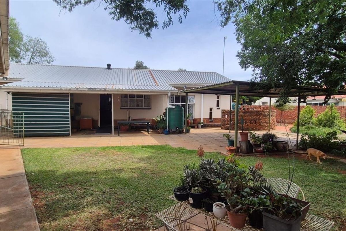 A spacious rear garden featuring a paved patio area, a covered outdoor structure, and a well-maintained lawn, providing a functional outdoor living space.