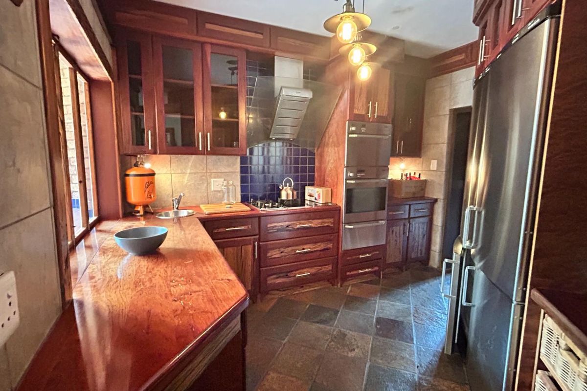 A rustic kitchen featuring dark wood cabinetry, stone tile flooring, built-in oven, extractor fan, and a long wooden countertop with an integrated sink.