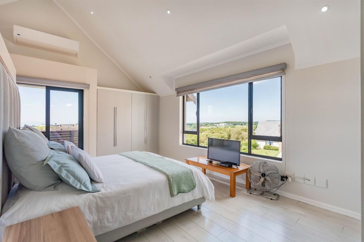 A bright, spacious bedroom featuring vaulted ceilings, built-in cabinetry, large windows with scenic views, and a wall-mounted air conditioning unit.