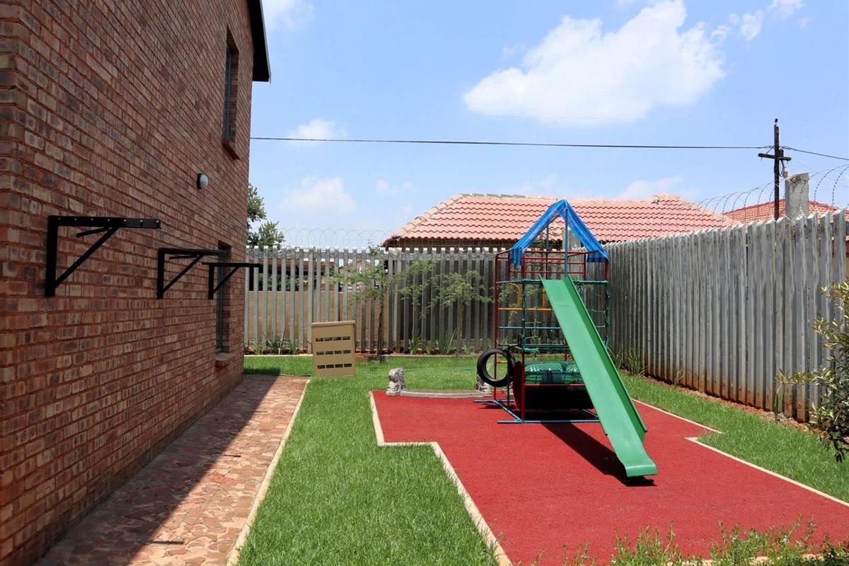 A side garden area featuring a brick-paved walkway, a grass lawn, and a dedicated play area with a slide and climbing frame.