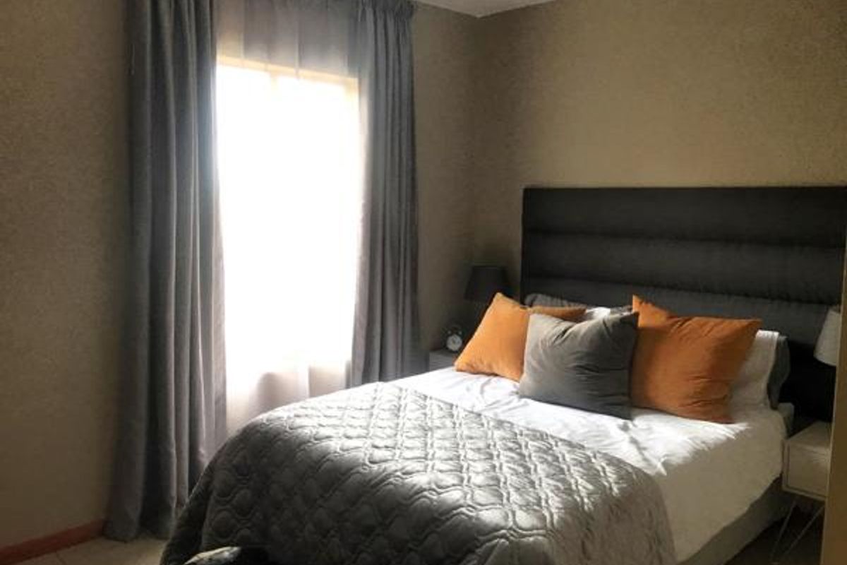 A cozy bedroom featuring neutral wall finishes, floor-length curtains, and a built-in headboard area, providing a comfortable and functional sleeping space.