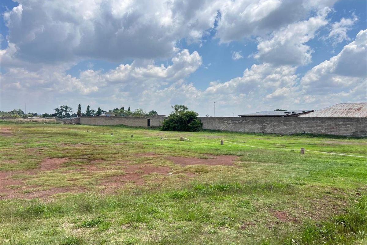 A vacant residential plot featuring open grass land, boundary markers, and a perimeter wall, offering a clear space for future development.
