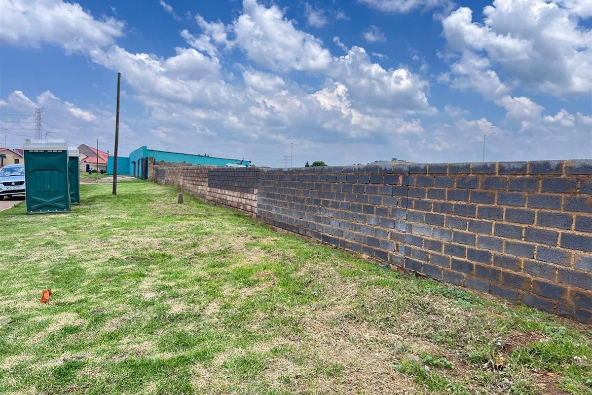 A vacant residential plot featuring a long perimeter brick boundary wall and open grass area.