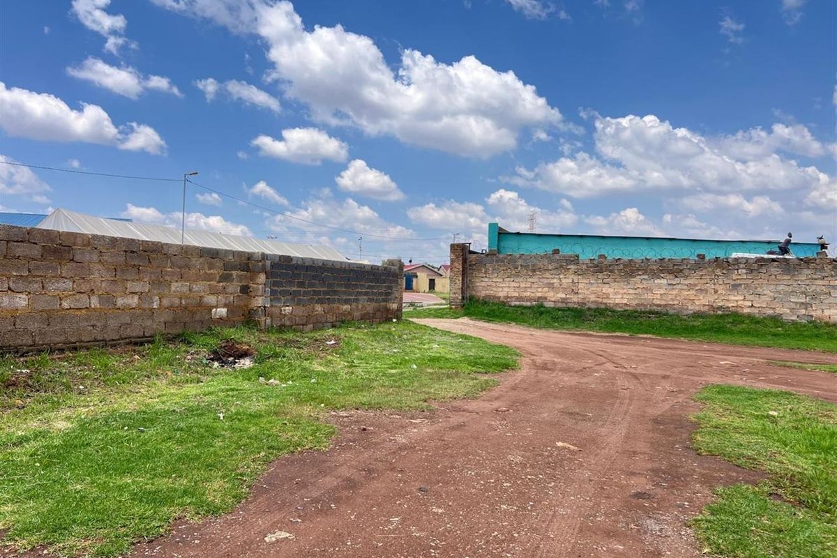 A view of a vacant residential plot featuring perimeter brick walls and an unpaved access road.