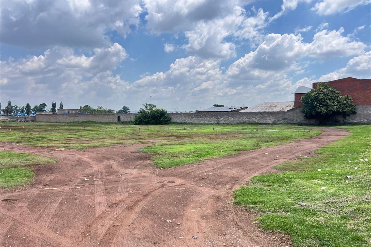 A view of a vacant residential plot featuring a perimeter boundary wall and open grassed area.