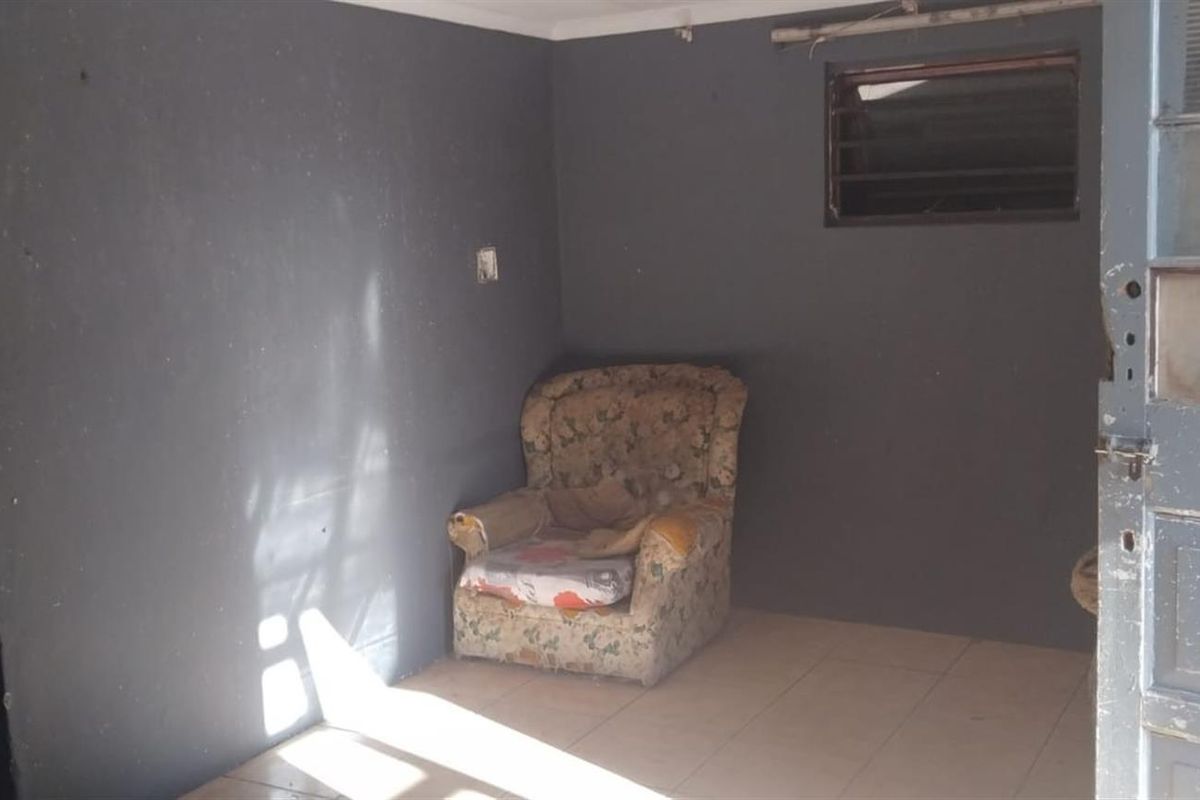 A sparsely furnished living area featuring dark painted walls, tiled flooring, and a small louvre window, requiring cosmetic updates to improve its appeal.