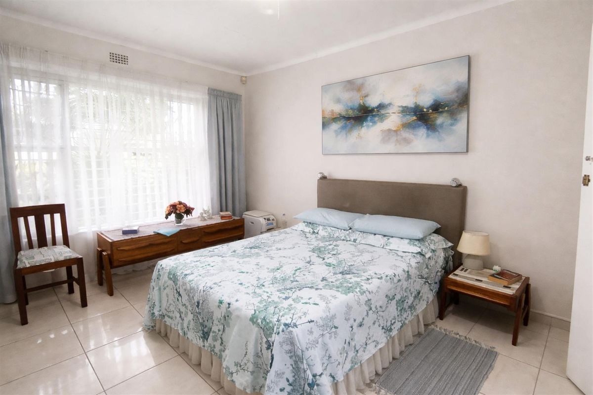 A well-lit bedroom featuring neutral tiled flooring and large windows, providing a comfortable and functional living space.