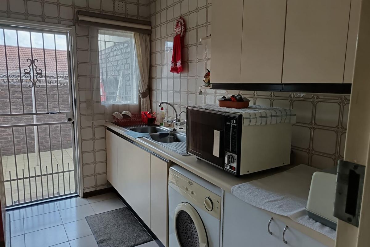 A functional kitchen featuring built-in cabinetry, tiled splashbacks, and direct access to an outdoor area through a security gate.